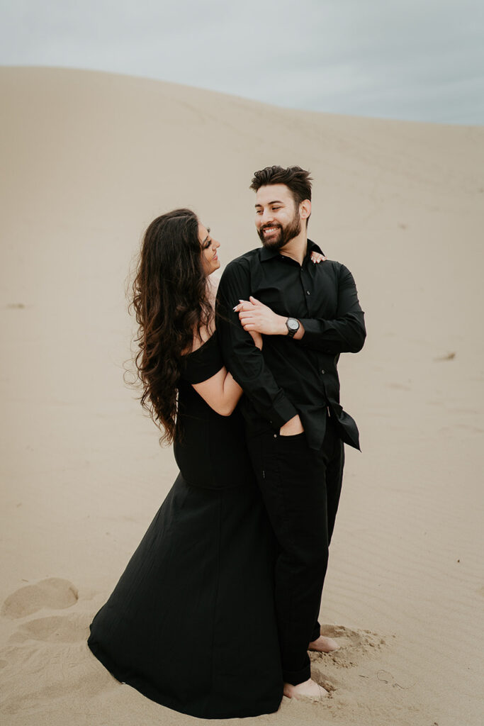 A newly engaged couple dressed in all black looking lovingly into each other's eyes.