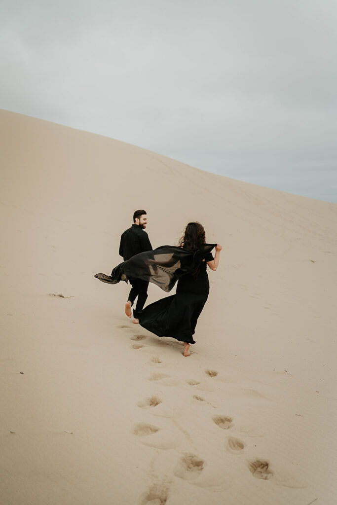A couple walking, the girlfriend's dress flowing in the wind, walking on the Oregon sand dunes. 