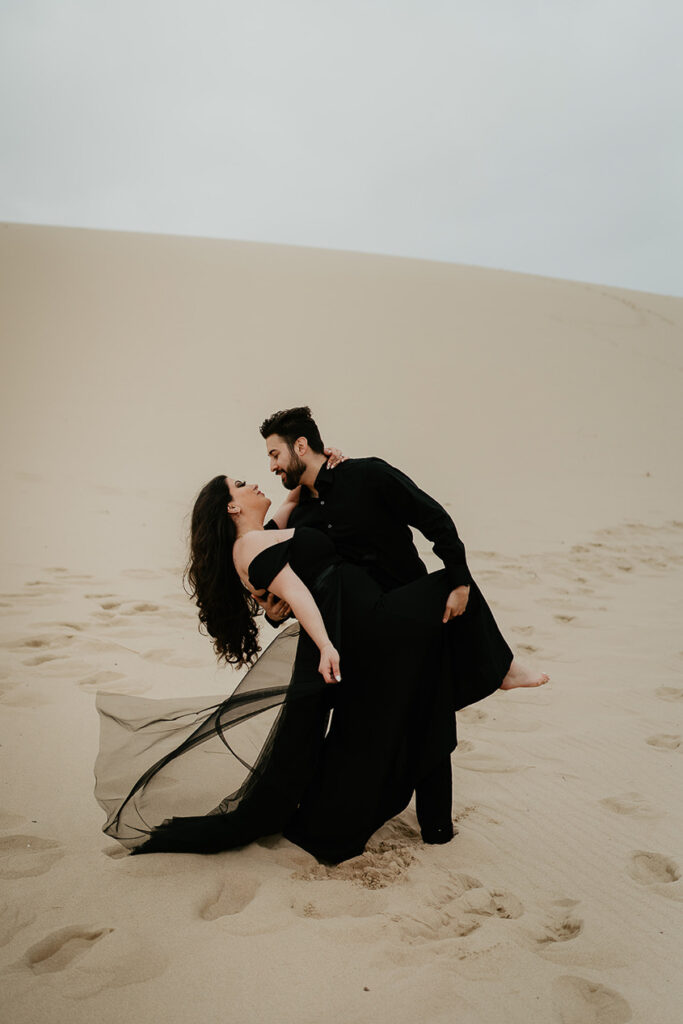 A couple dressed in all black dancing on sand dunes. 