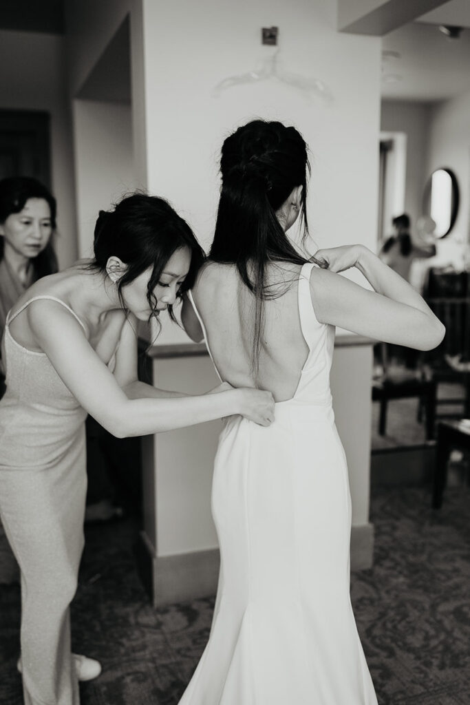 A black and white photo of Judith getting her dress adjusted. 