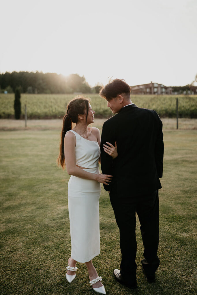Joshua and Judith looking lovingly into each other's eyes while the sun sets and with a vineyard in the background.