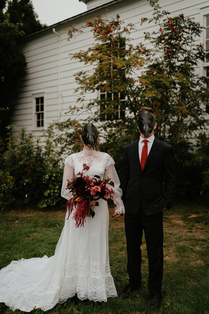 A couple wearing bird masks holding hands in front of a chapel. 