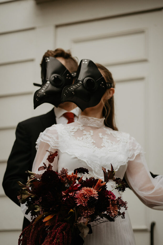 A couple in bird masks dancing in front of a white building. 