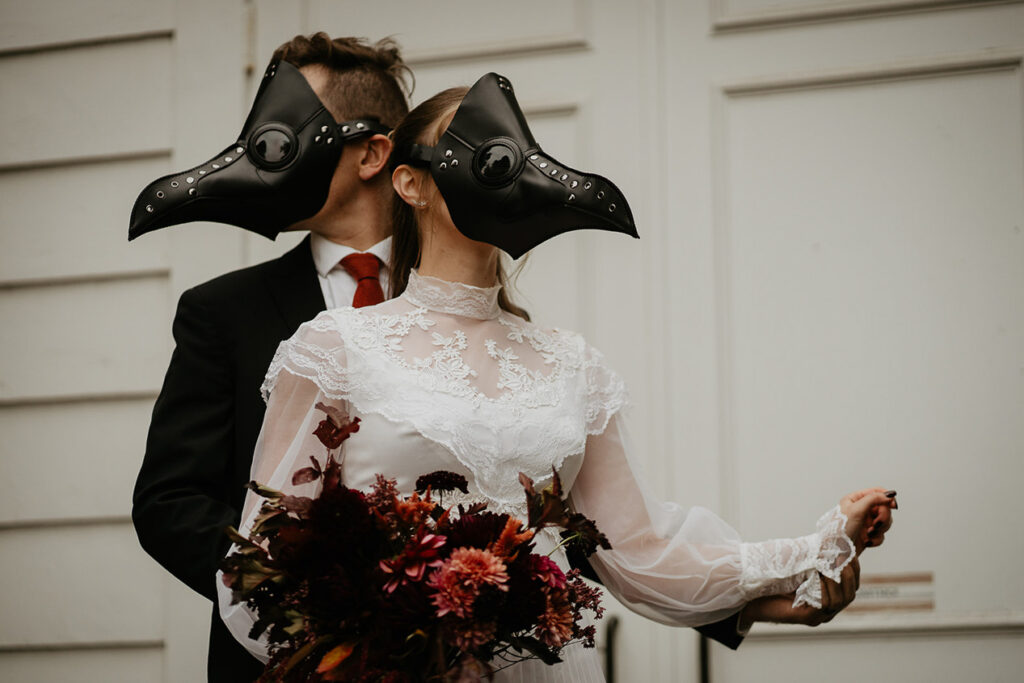 A couple in bird masks dancing in front of a white building. 
