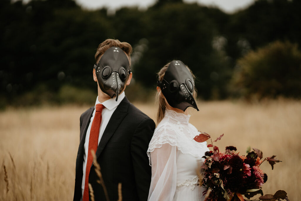 A couple wearing bird masks standing in a field. 