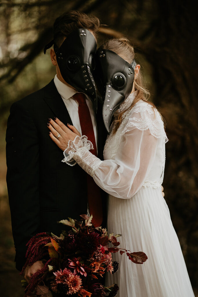 A couple wearing bird masks holding each other in the forest. 