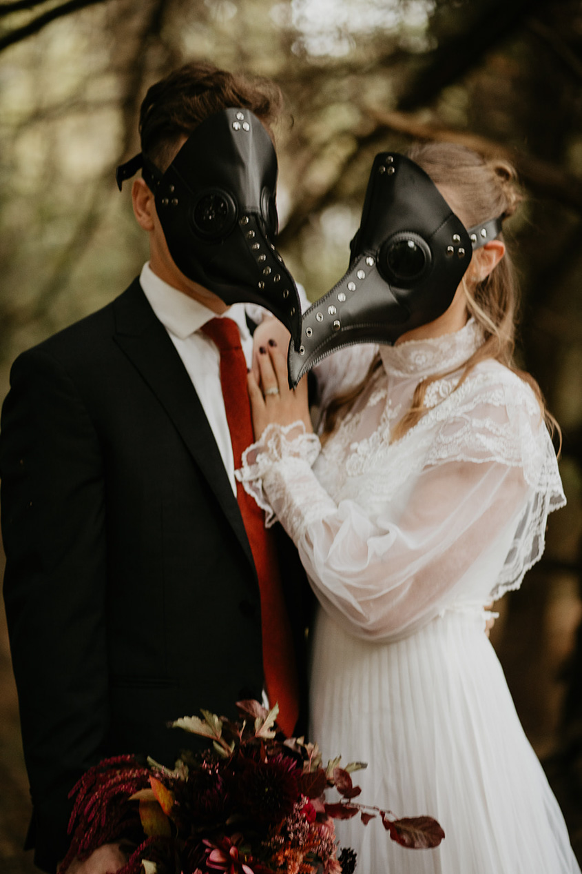 A couple wearing bird masks under a tree.