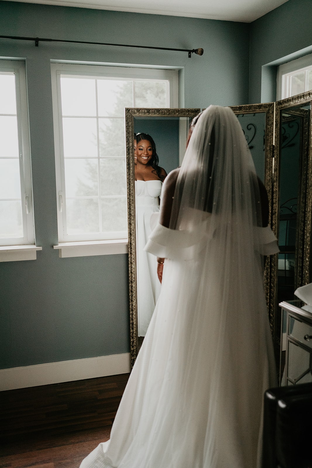 Bride smiling in front of the mirror while wearing her white wedding dress and veil