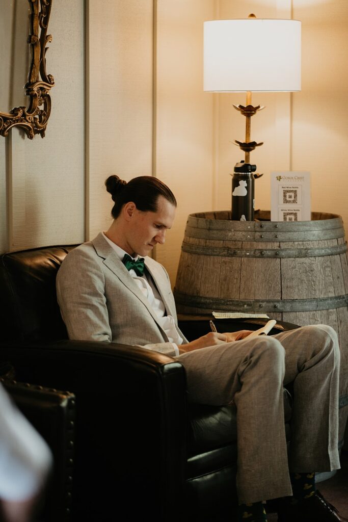 Groom sitting in a leather chair writing his personal vows
