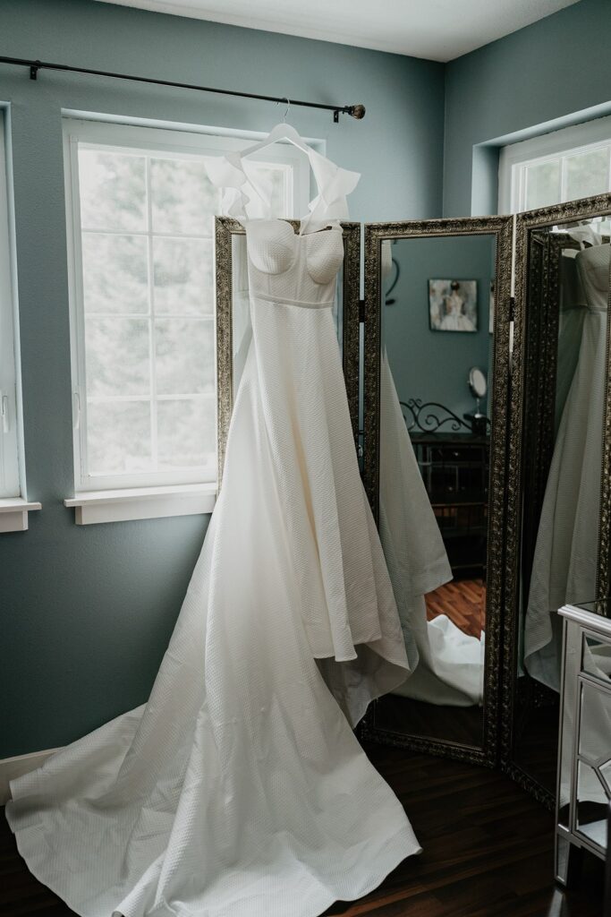 White wedding dress hanging from a curtain rod in a blue room