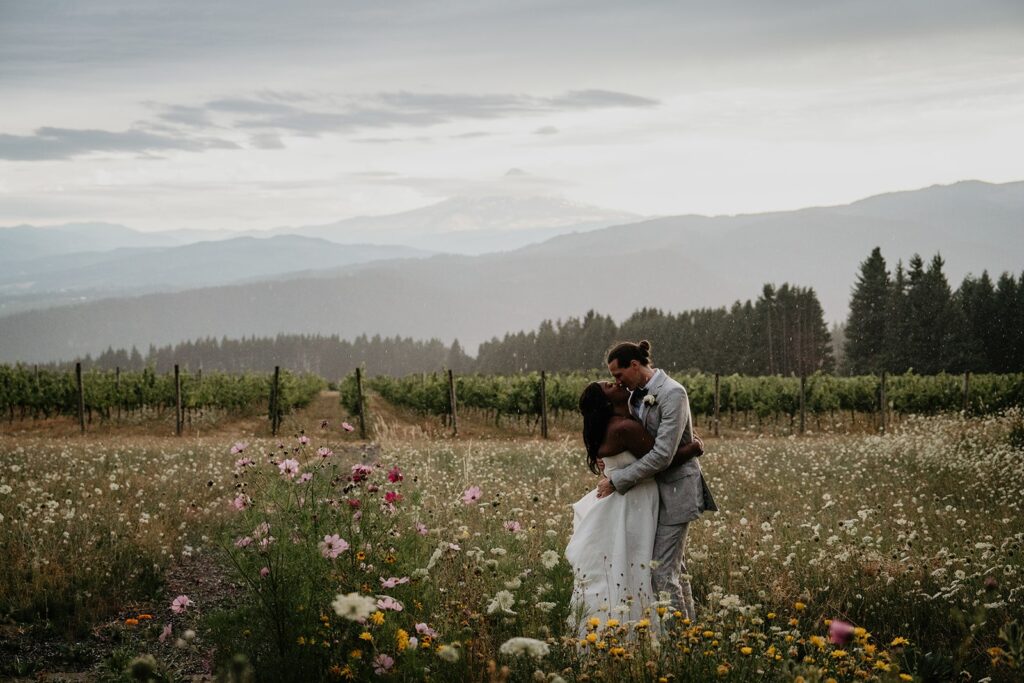 Bride and groom kiss in a wildflower field during couple photos at Gorge Crest Vineyards wedding