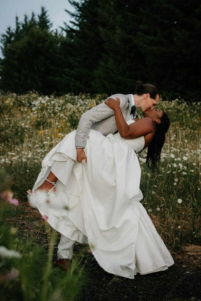 Groom dips bride for a kiss during couple photos in a wildflower field at Gorge Crest Vineyards wedding