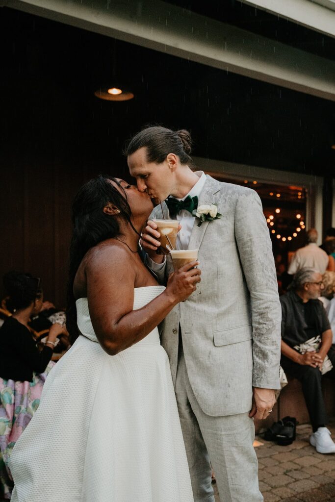 Bride and groom kiss while holding ice coffees at their winery wedding in Washington