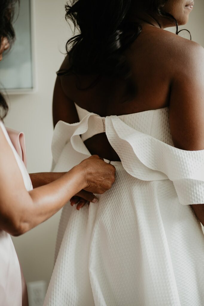 Bride getting zipped into white wedding dress with ruffled sleeves