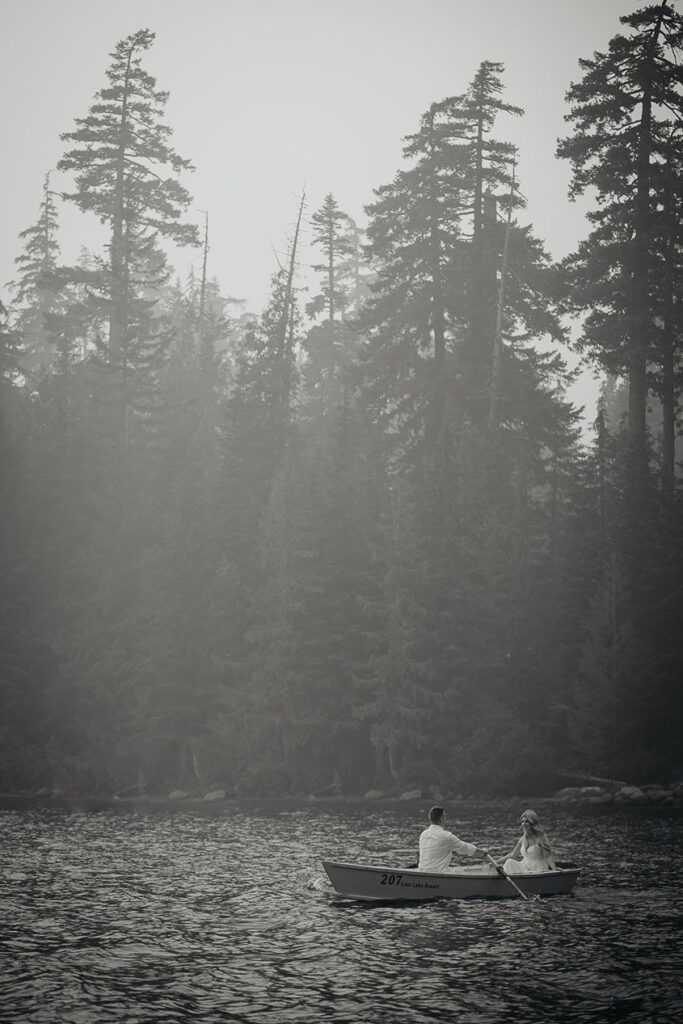 A black and white photo of the couple in a row boat on Lost Lake with pine trees in the background. 