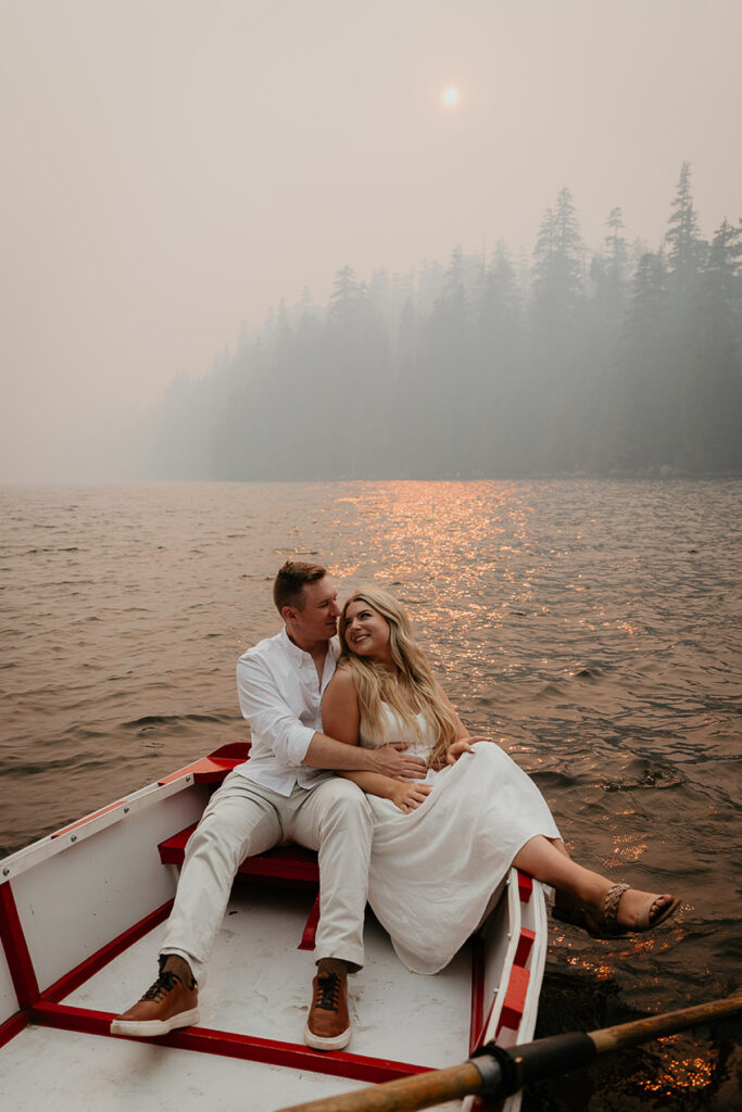 A couple hugging on a row boat on Lost Lake, with smoke and pine trees in the background. 