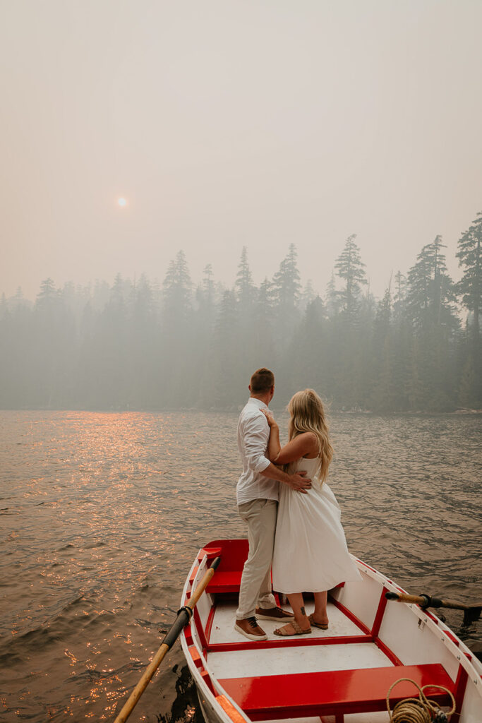 A couple looking out at the smoke-filled sky, standing on a row boat. 