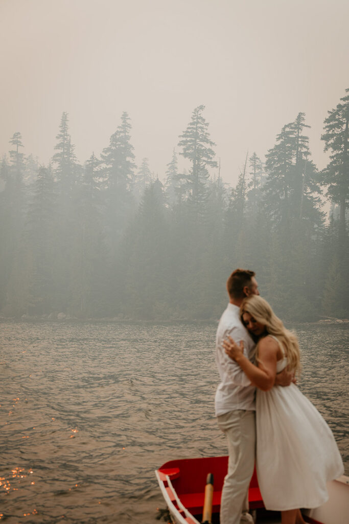 A couple standing on a rowboat in the water and hugging. 