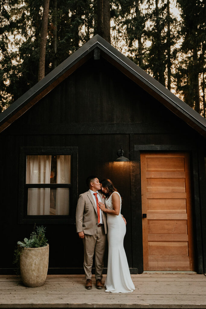 The couple holding each other under an A-frame house. 