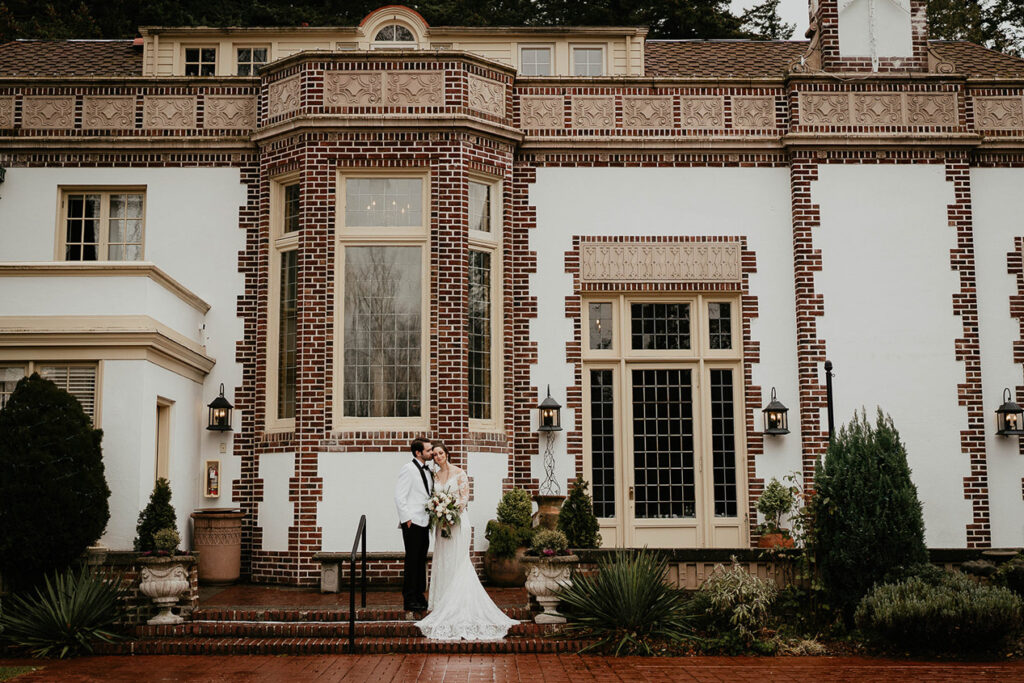 The bride and groom standing in front of a manor. 
