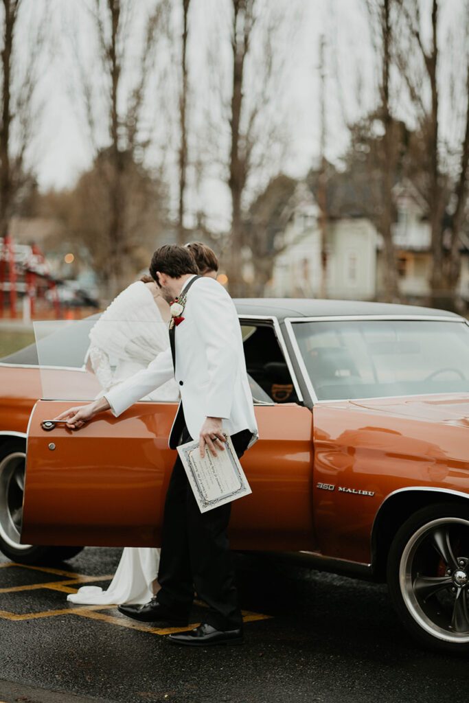 The bride and groom entering a vintage orange car. 