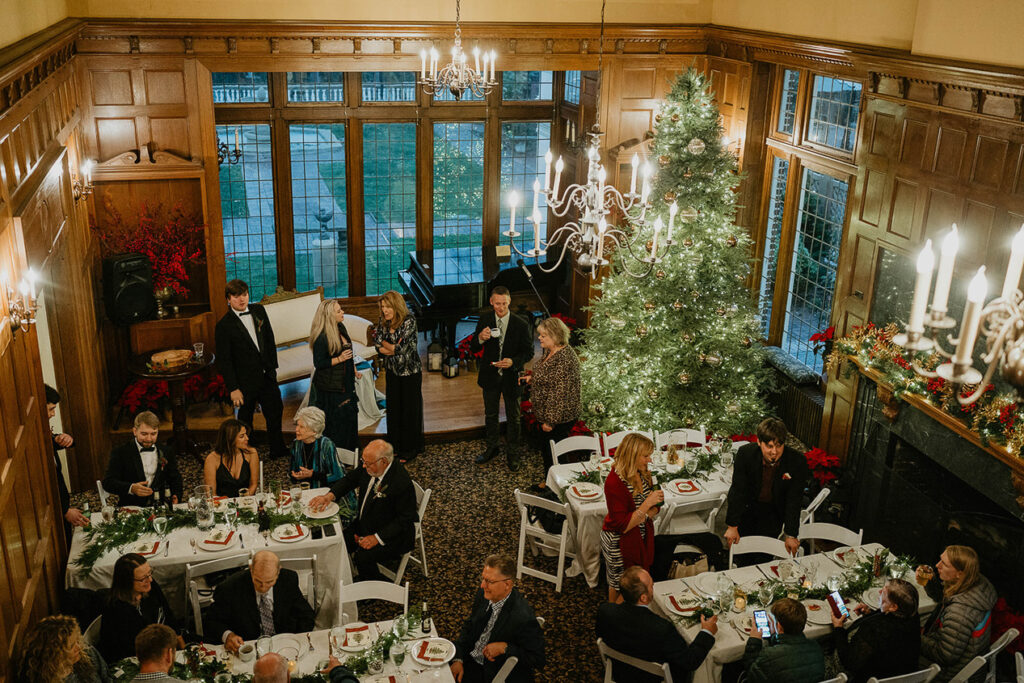 A birds-eye view of the dinner party, with guests, plates of food, and a large Christmas tree. 