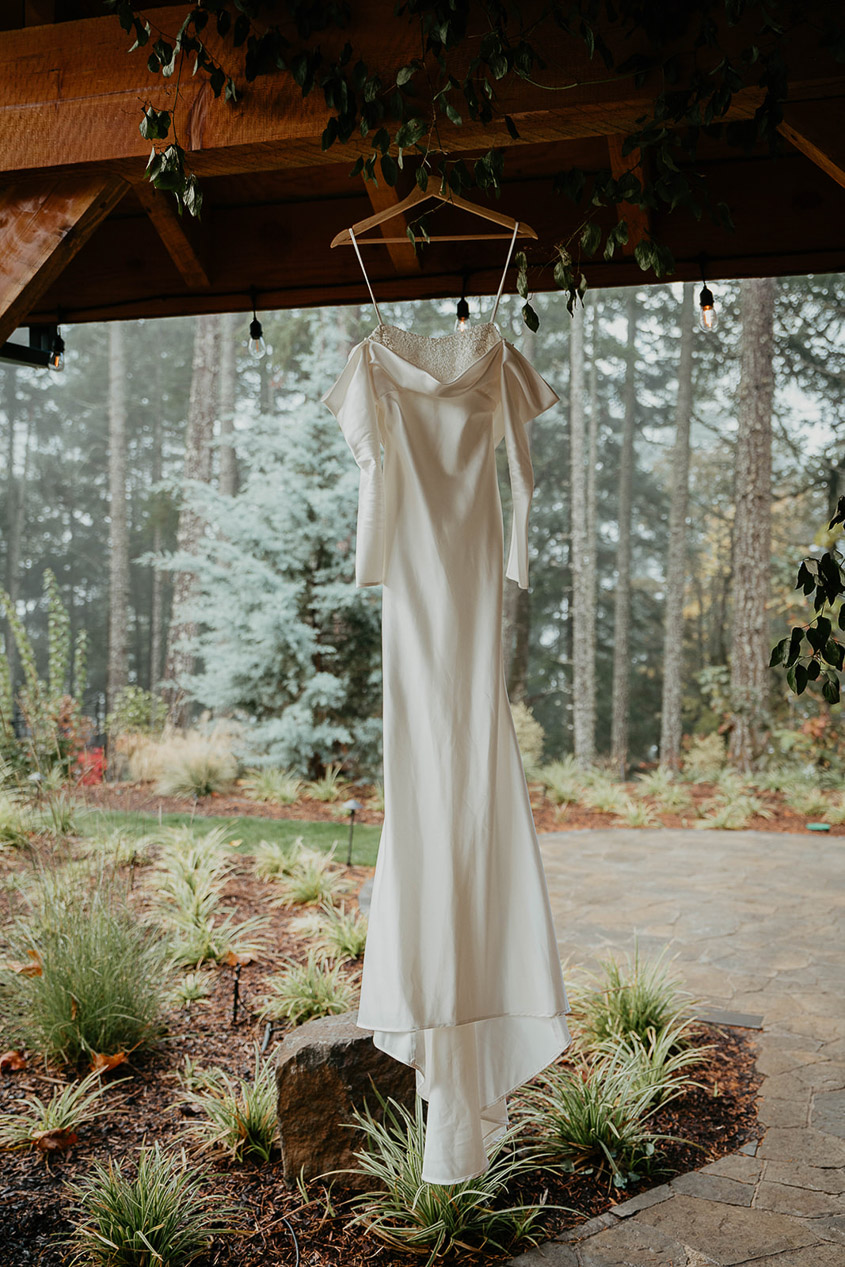 The wedding dress hanging outside with a forest in the background. 
