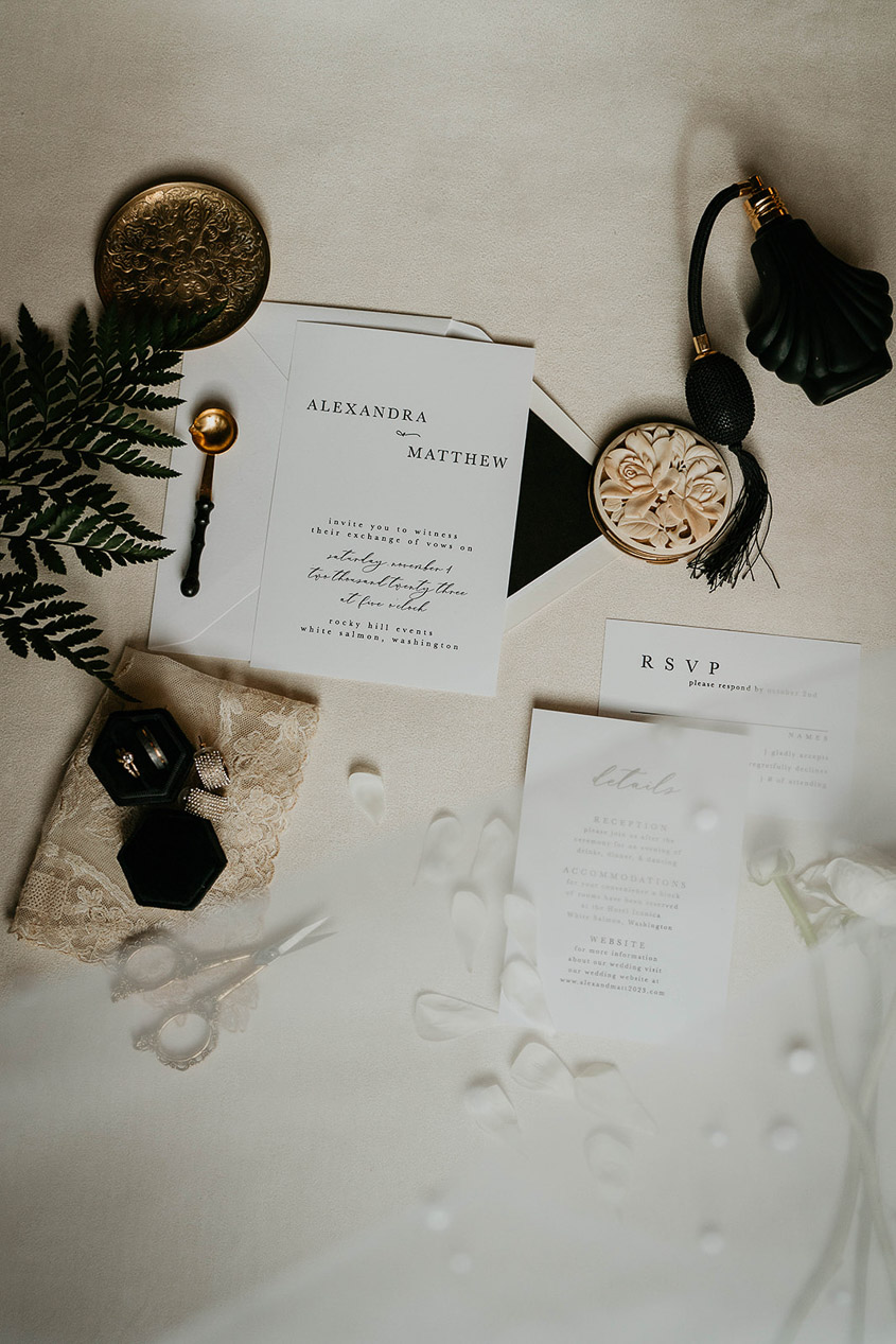 Wedding details, including a wedding invite, rings, and perfume. 