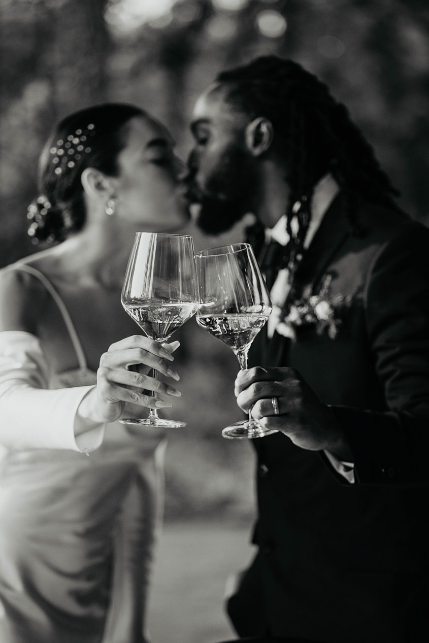 The bride and groom toasting wine glasses while kissing. 