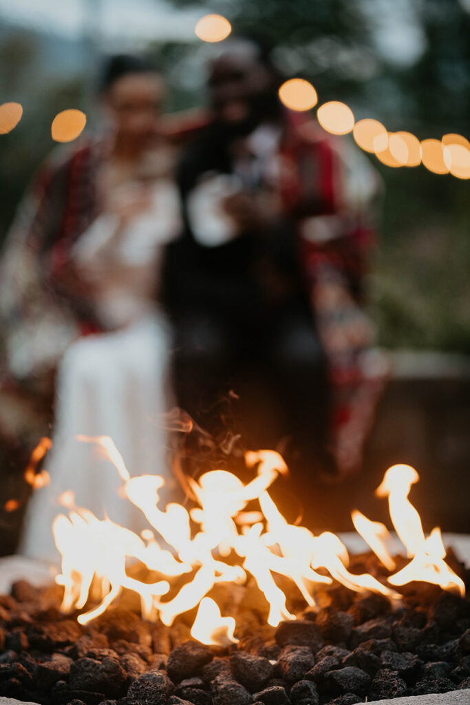 A fire with the bride and groom in the background under a blanket. 