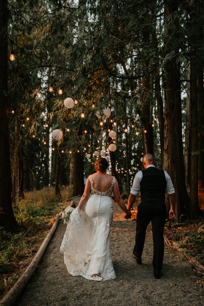 Bride and groom hold hands while walking through the forest at CedarVale Events wedding venue in Oregon