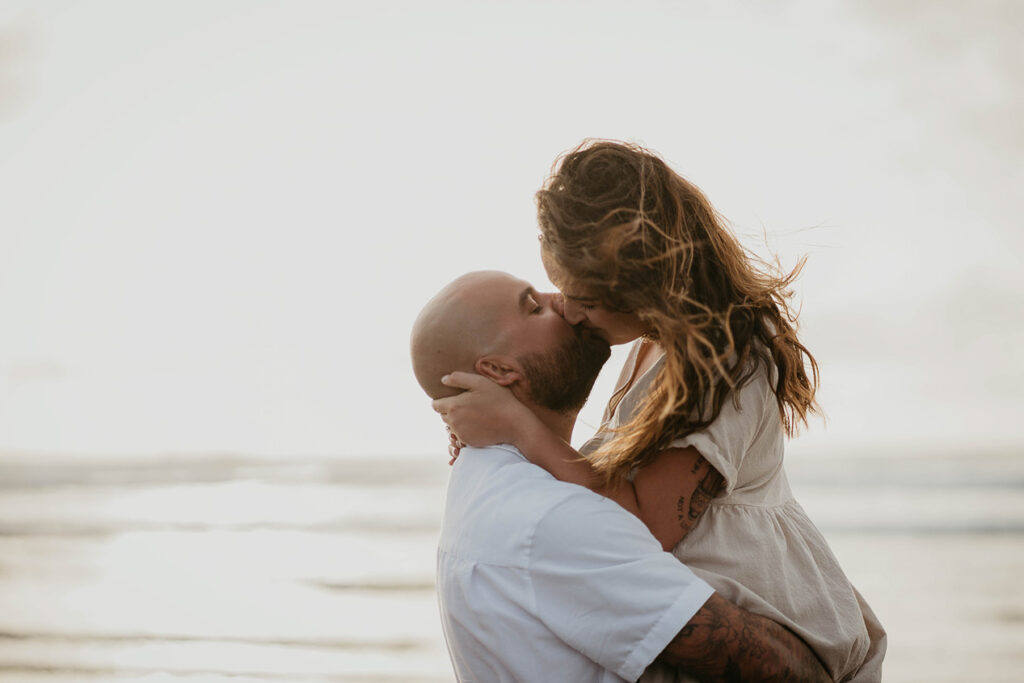 a newly engaged couple kissing with the beach in the background. 