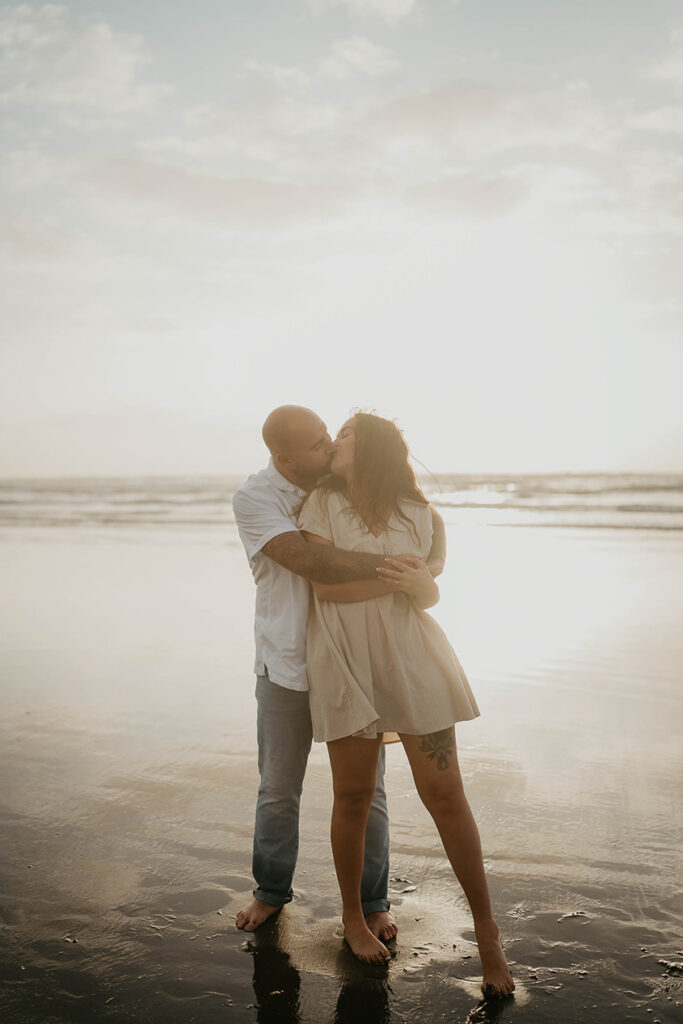 a newly engaged couple kissing at Cannon Beach with the Pacific Ocean in the background. 