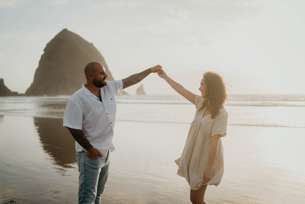 a newly engaged couple holding hands at Cannon Beach with Haystack Rock in the background. 