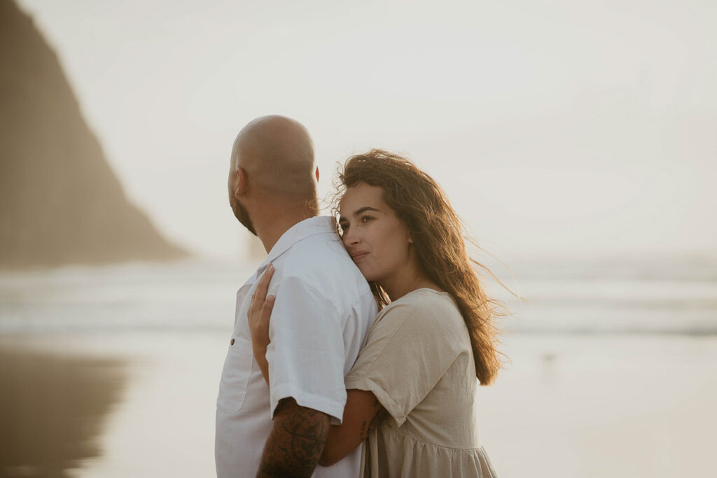 a newly engaged couple holding each other with Haystack Rock in the background. 