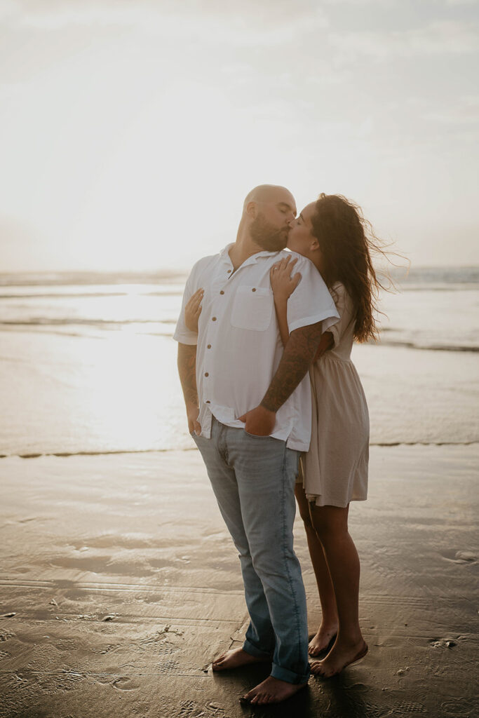 a newly engaged couple kissing with the Pacific Ocean in the background. 