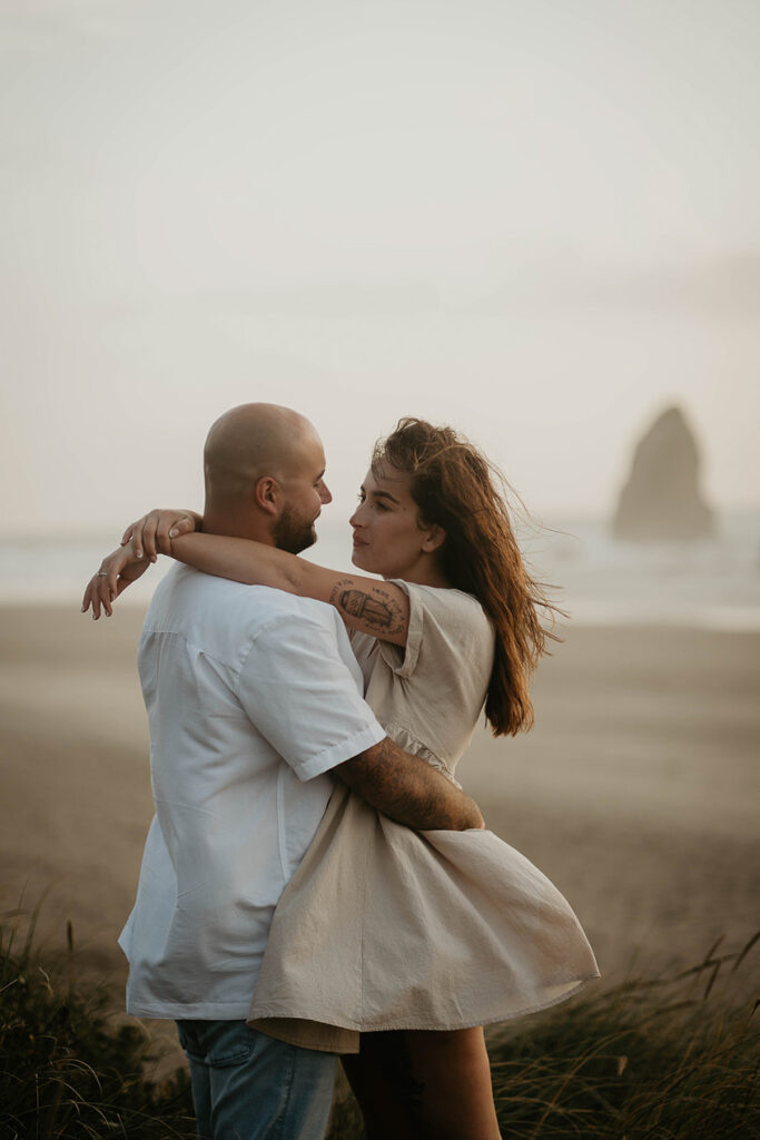 a newly engaged couple dancing among beach grass with Haystack Rock in the background. 