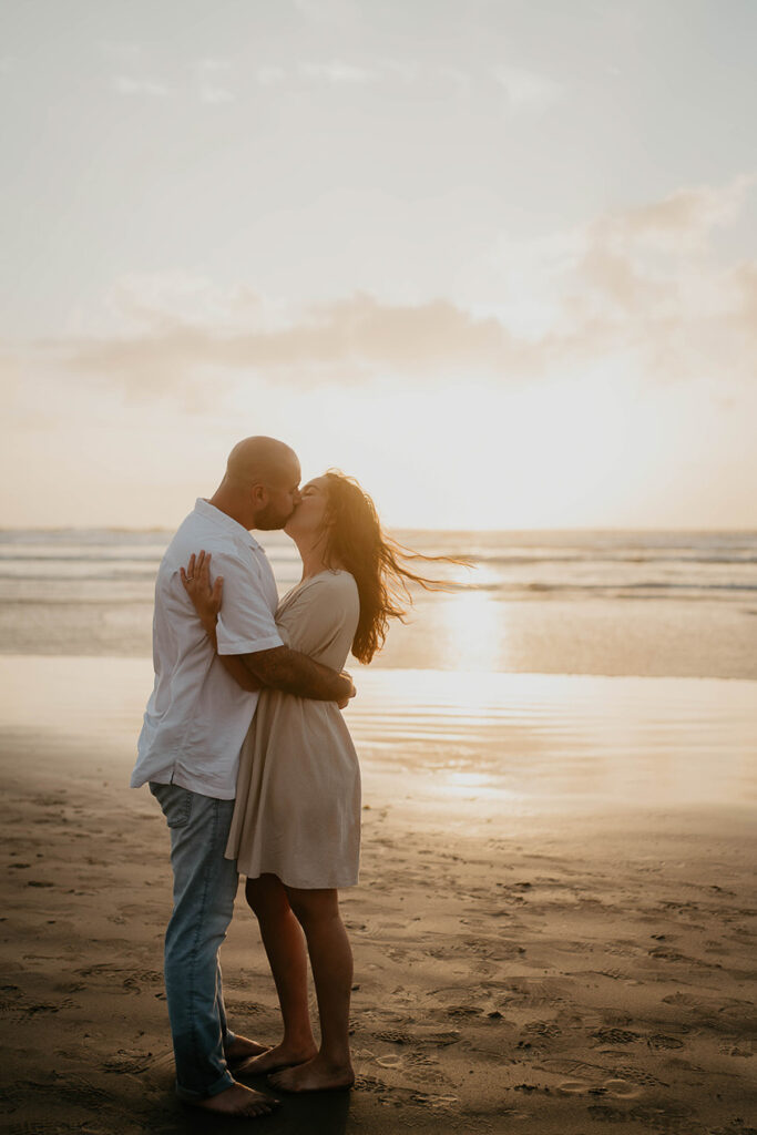 a newly engaged couple kissing as the sun is setting at Cannon Beach. 