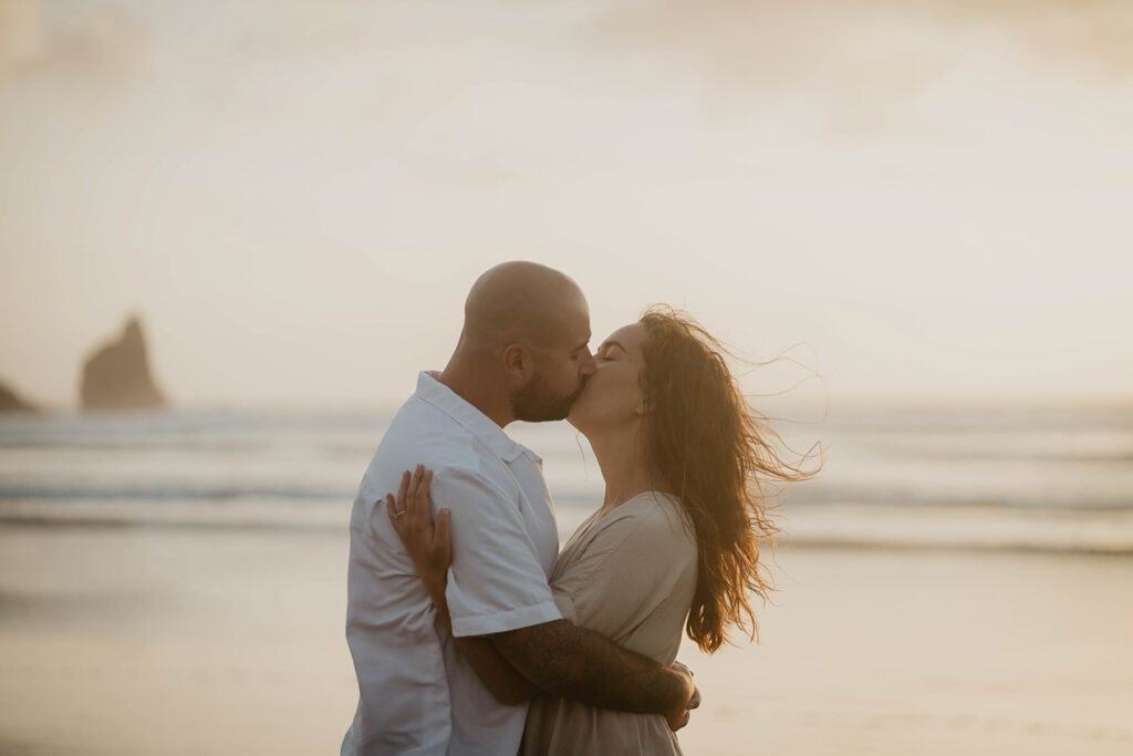 a newly engaged couple kissing as the sun is setting at Cannon Beach. 