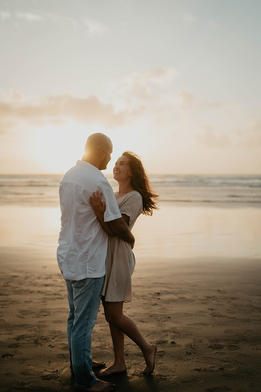 a newly engaged couple hugging as the sun is setting at Cannon Beach. 