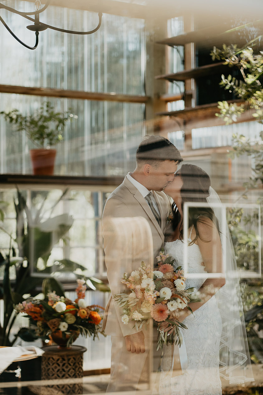the bride and groom kissing surrounded by potted plants. 