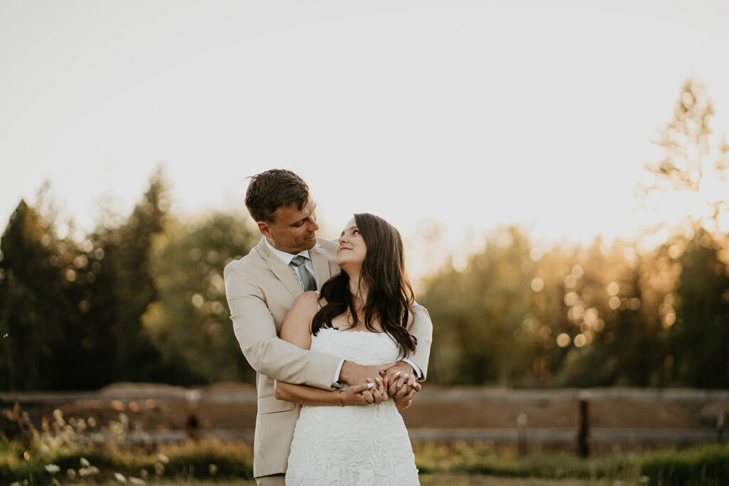 the newlyweds holding each other in a field at sunset. 