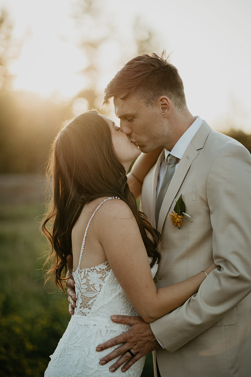 newlyweds kissing in a field as the sun sets. 