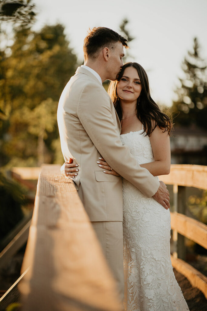 newlyweds hugging and kissing on a bridge during golden hour. 