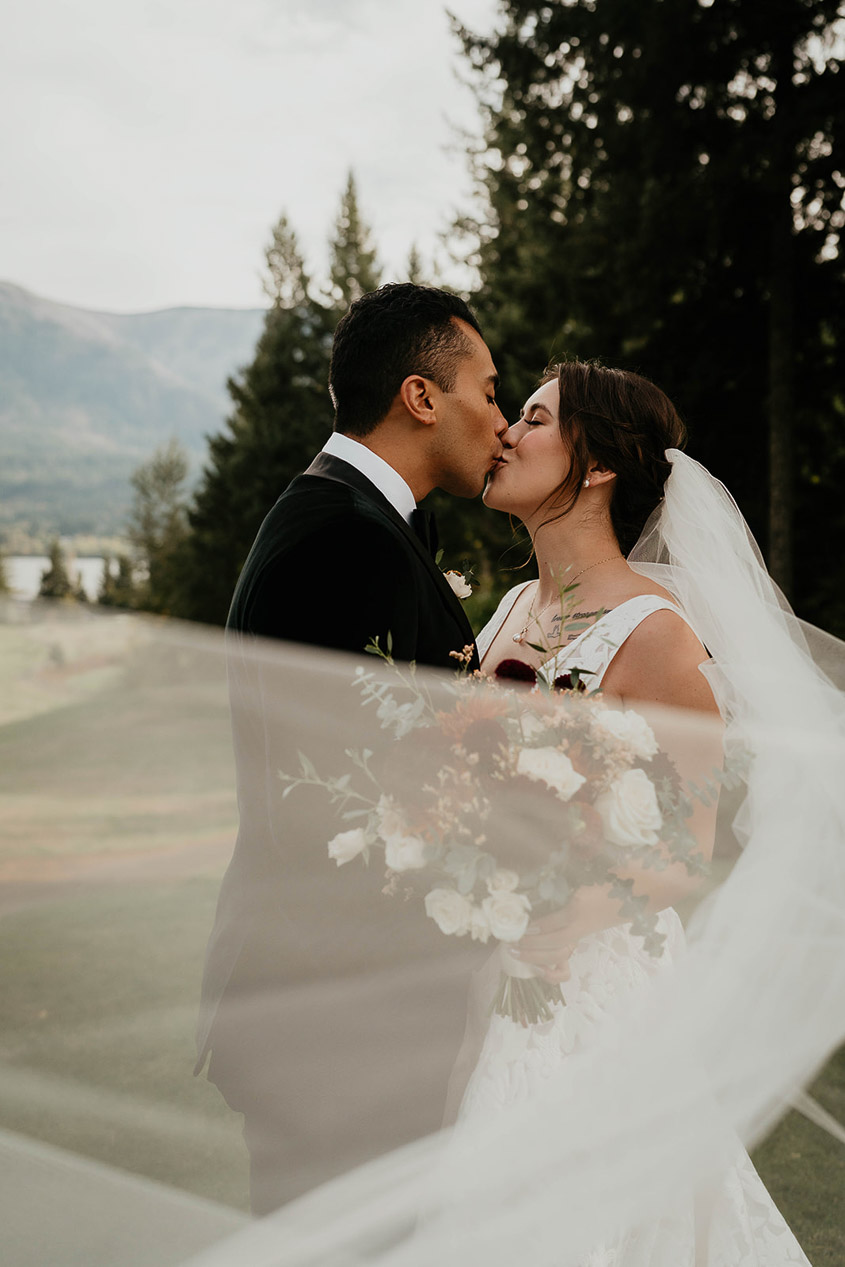 A couple kissing on their wedding day, with the bride's vail waving in the wind.