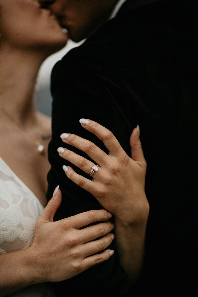 a closeup on the bride's wedding ring and her and the groom are kissing. 