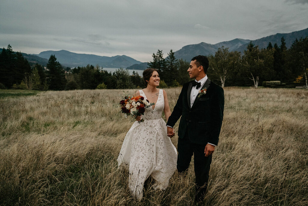 The newlyweds walking through a grassy field with the Columbia River in the background. 