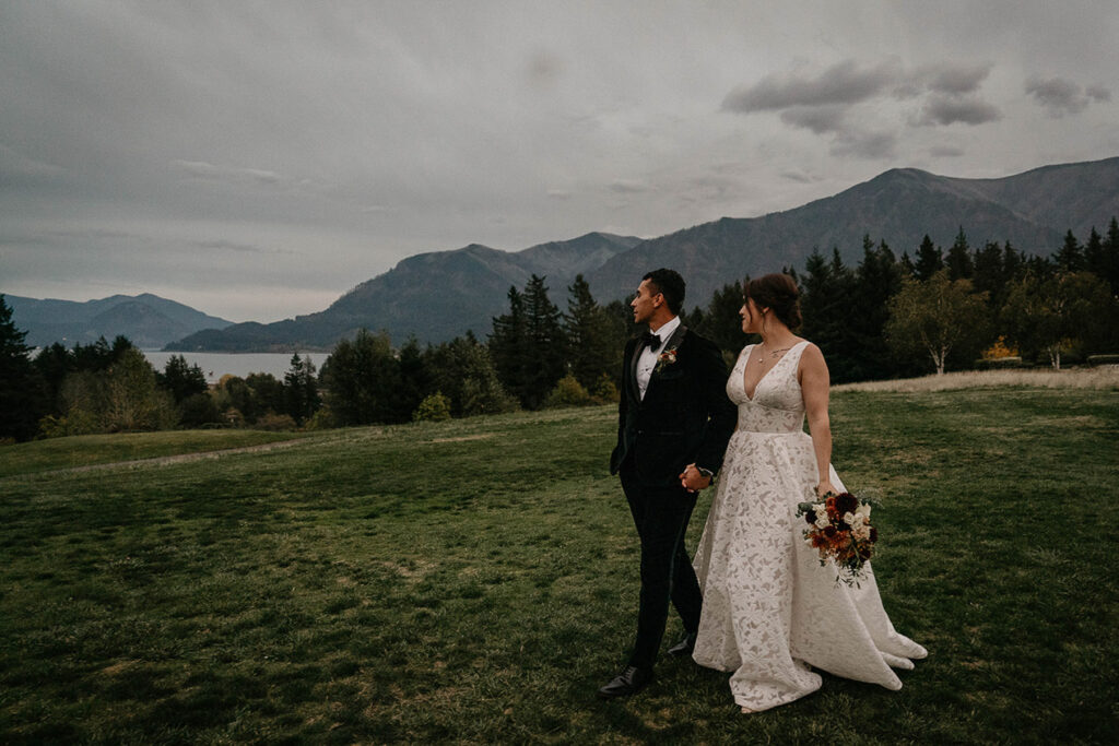 the newlyweds holding hands walking through a grassy field at Skamania Lodge. 