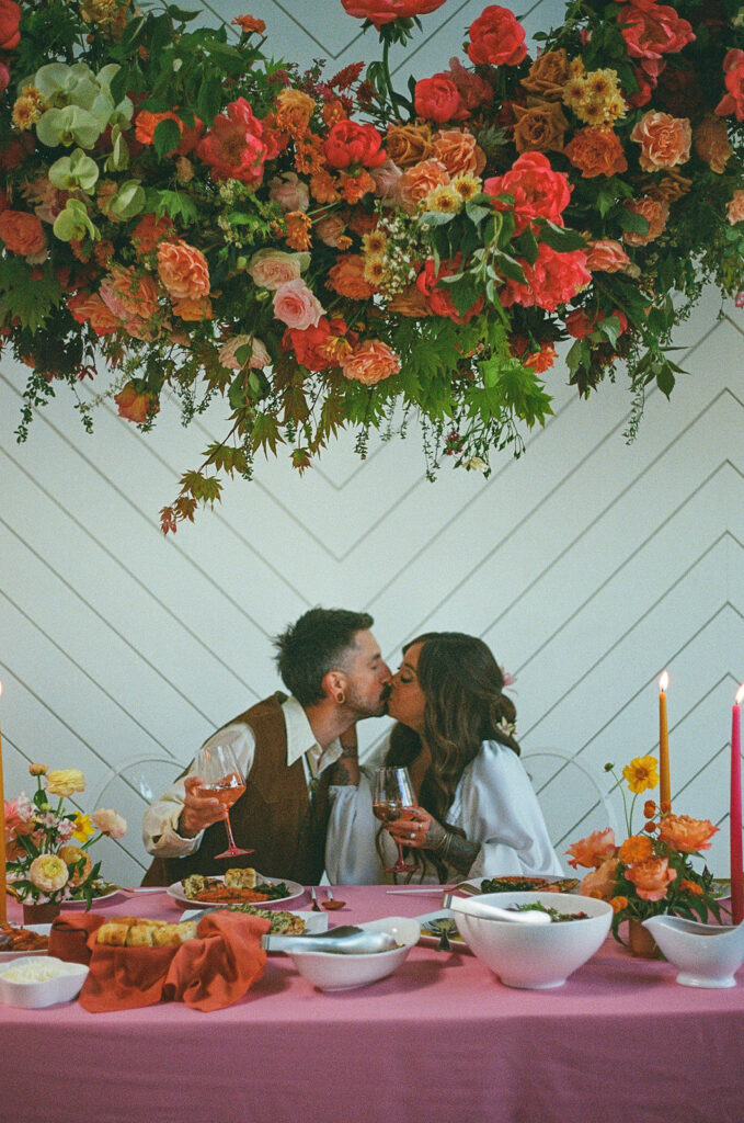 Film wedding photography with bride and groom kissing at their hot pink wedding reception table
