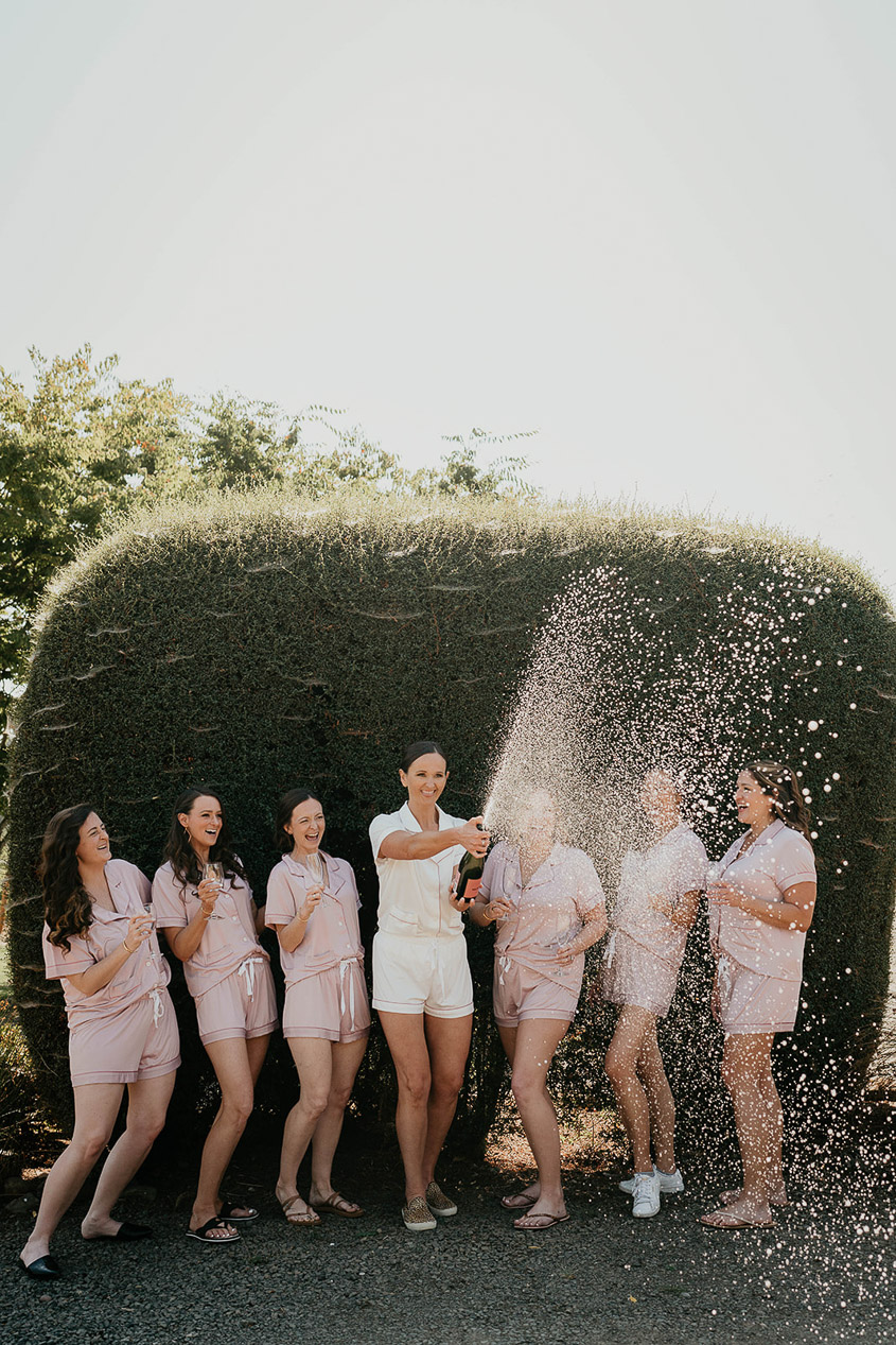 The bride spraying a bottle of champagne with her bridesmaids. 